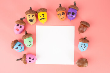 Whimsical painted acorns with different faces, circle arrangement, blank white square, pink background, colorful craft, autumn decoration, nature art, creative, educational, playful