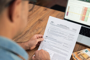 Naklejka premium Real estate agent carefully checks W-9 form confirming TIN and address for reporting commissions earned from property sales on table with laptop and euro bills
