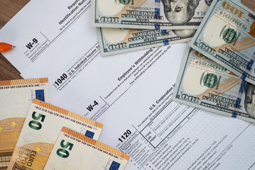 Dollar and euro banknotes placed on different tax forms mandatory for businesses and taxpayers to report annual income in compliance with law at workplace in office