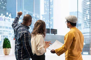 Corporate team reviewing architectural plans for a new office, discussing the building layout and the blueprints, potential investment opportunity in real estate during an office tour.