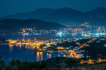 Fototapeta premium A panoramic view of a coastal town at night, with twinkling lights reflecting off the calm waters of the bay. The town is nestled between rolling hills