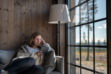 A beautiful woman relaxes on a sofa while reading on her E-Reader, in a comfortable wool vest...