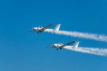 Stunt aerobatic plane performing stunts in blue sky with smoke trail. Concept of teamwork, collaboration, coordination, trust, precision, difficulty, challenge, speed, synergy