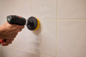 A man is using an electric drill that has a brush attachment to thoroughly clean tiles