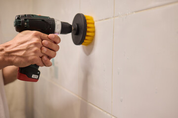 A man is using an electric drill that has a brush attachment to thoroughly clean tiles
