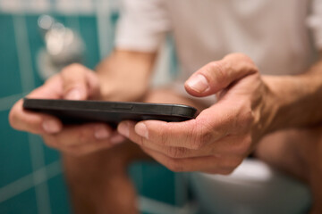 A person casually using their smartphone while seated on the toilet in a modern bathroom