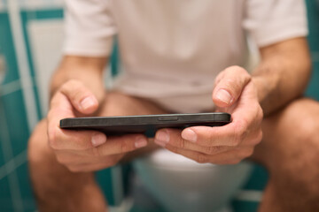 A person casually using their smartphone while seated on the toilet in a modern bathroom