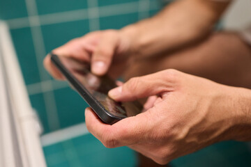 A person casually using their smartphone while seated on the toilet in a modern bathroom