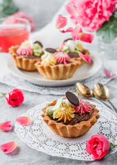 Set of mini basket cakes or sand tartlets cake with cream on light background with rose flowers. Sweets, dessert and pastry, top view, selective focus
