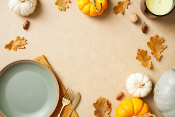 Autumn flat lay with pumpkins, dry leaves, acorns, and a candle on beige table. Seasonal decor, Thanksgiving, cozy home setting