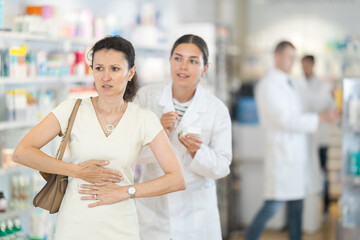 Young female pharmacist advising medicine for stomach pain to adult woman at pharmacy