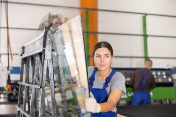 Fototapeta premium Portrait of woman in blue overalls with window panes in a glass workshop