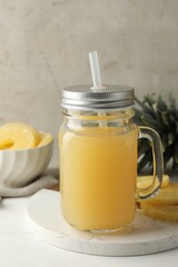 Tasty pineapple juice in mason jar and fresh fruits on white wooden table against grey background, closeup