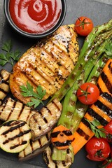 Delicious grilled vegetables and chicken breast served with sauce on grey table, top view
