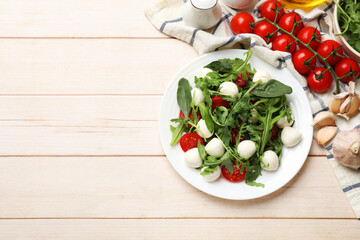 Tasty salad with arugula, spinach, mozzarella cheese and tomatoes on wooden table, flat lay. Space for text