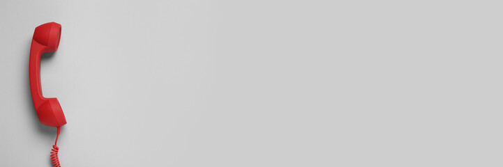 Red corded telephone handset on grey background, top view. Banner design with space for text