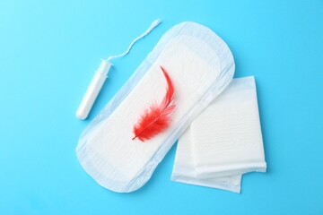 Menstrual pad with red feather and tampon on light blue background, top view