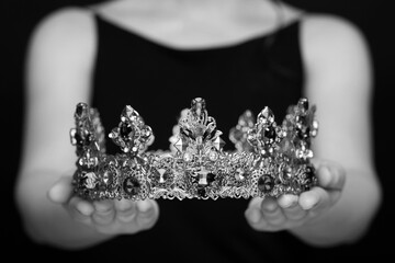Woman holding luxury crown, closeup. Black-and-white photo