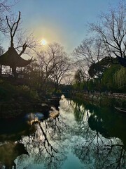 Tranquil River Scene with Reflections of Bare Trees and Setting Sun near a Traditional Pagoda