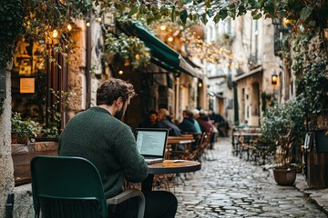 A man works on his laptop at a charming café in a historic cobblestone alley adorned with fairy lights during evening hours. Generative AI