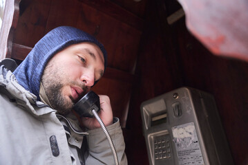 Young man testing the line of an old payphone in a phone booth. Nostalgia for old technologies.
