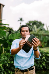 Fototapeta premium A Southeast Asian man is putting money into his wallet, focusing on the task. T