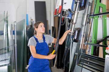 Experienced young female technician confidently operating vacuum lifting machine to move glass...