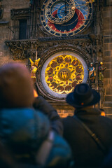 Tourists watching the Prague Astronomical Clock and its multiple details. In the foreground there is a man with a hat.