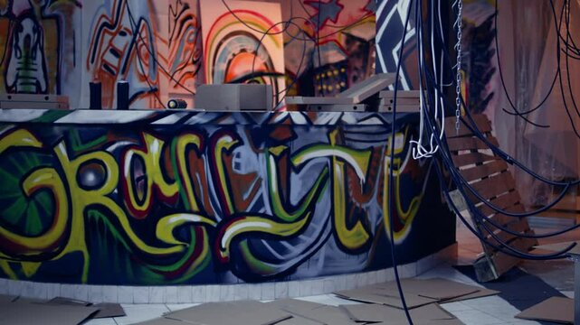 Desolate headquarters used by gang members with graffiti drawings sprayed on walls. Rubble in ghetto hideout after criminals rushed to evacuate place, dolly in camera shot
