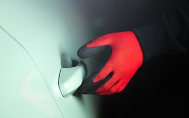 Man's gloved hand holding a screwdriver, attempting to pry open a car door handle. The image...