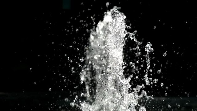 Water splashes from a fountain against a black background create a striking contrast, highlighting dynamism and freshness. An ideal image for design, web development, and decor.
