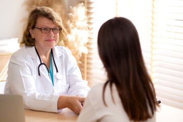 Senior woman doctor examining elderly while holding arm for pulse sitting in modern medical office,...
