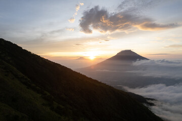Obraz premium A breathtaking sunrise over two majestic volcanoes with dramatic clouds. Perfect for travel, adventure, and nature themed projects.