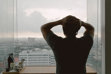 Lonely single asian man looking out to through the windows of apartment.