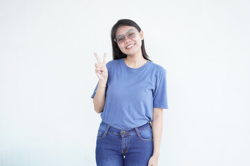 Beautiful Asian woman smiles warmly while flashing a peace or victory sign against a bright white...