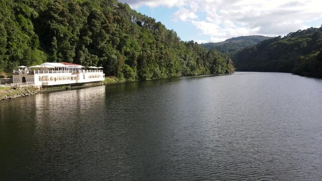 4k drone view of a tranquil health resort set against lush, forested hills, peacefully overlooking a calm river, offering a perfect retreat surrounded by nature in Cortegada, Galicia, Spain
