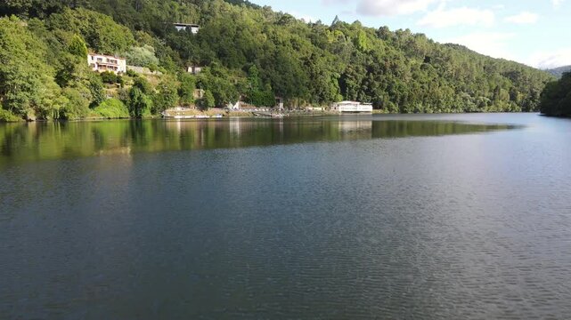 Drone approximation towards Cortegada village gradually revealing its charming riverside luxury spa resort, surrounded by lush forests and nestled along the calm riverbank