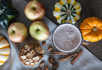 Hot chocolate in a glass mug paired with a spiced apple and almond muffin surrounded with pumpkins of various shapes