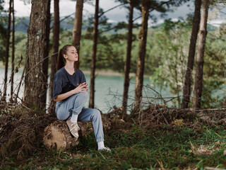 Thoughtful young woman relaxing by the lake, dressed casually in comfortable clothing, surrounded by trees in a serene outdoor setting Nature and tranquility concept