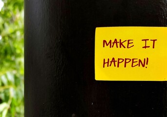 Yellow stick note on black wall with handwritten text MAKE IT HAPPEN!, idiom of self motivati on to...
