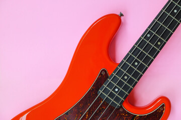Fototapeta premium Red electric bass guitar on a pink background. Close-up image.