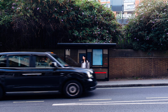 Young woman waiting at bus stop with black cab passing by - Powered by Adobe