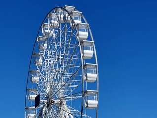 A towering Ferris wheel with white cabins against a vibrant blue sky. Perfect for amusement park, summer fun, and travel themes.