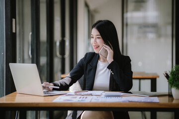 Beautiful Asian businesswoman talking on the phone using laptop in office