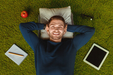 Student Lifestyle. Relaxed Guy Lying On Green Grass Carpet Among Digital Tablet, Notebook And...