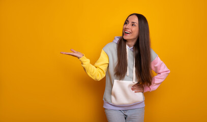 Happy woman stands against vibrant yellow background. She smiles confidently while gesturing with one hand, presenting or showing something, conveying positivity and openness