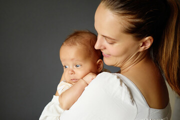 Smiling mother tenderly embracing little boy or girl nurturing him to create bond of care and affection woman sharing warm embrace with her infant daughter against gray wall with copy space