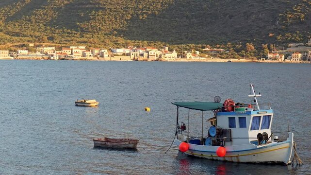 Anchored Greek Fishing boat floats in sunlit sea and mountain landscape