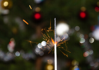 A bright sparkler on the background of a Christmas tree.