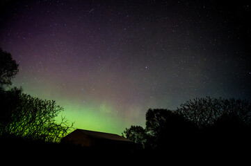 Starry night sky with green aurora borealis over barn roof
